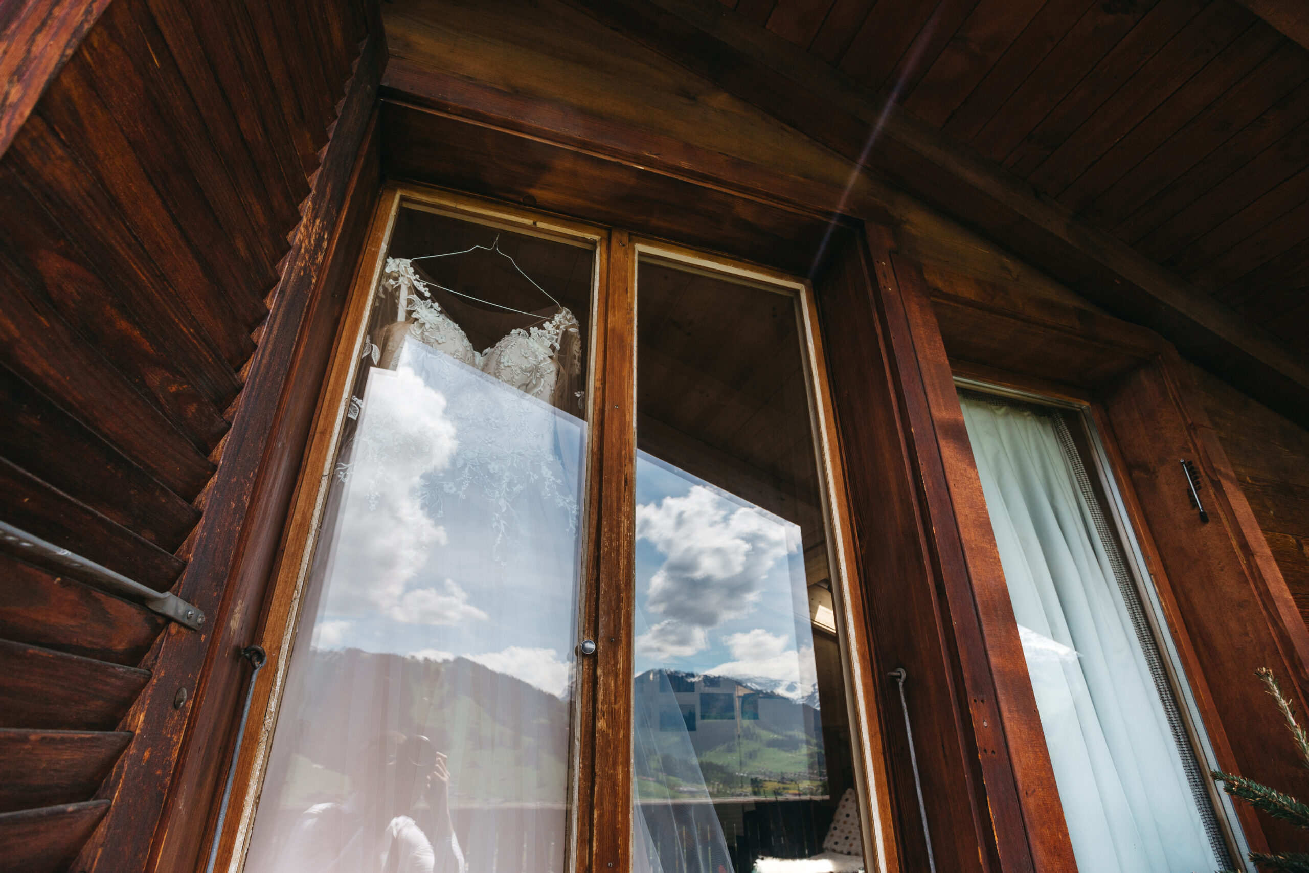 Bridal dress hangs up on a window in huge wooden hotel room Bridal dress hangs up on a window in huge wooden hotel room